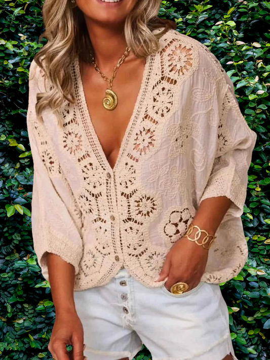 Woman wearing a beige lace top and denim shorts against a green leafy background